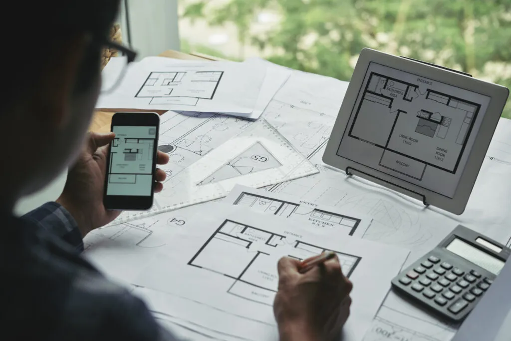 Arquiteto analisando plantas digitais em tablet e smartphone para projetos do Mercado Imobiliário em 2026.