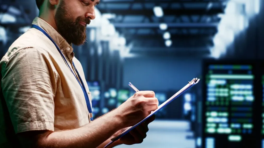 Homem em um data server anotando informações numa prancheta